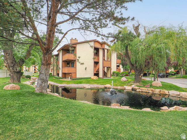 6852 Countrywoods Circle, Unit 5D Midvale, UT 84047 - Photo 1 of 50 Lush green lawn with a rock-lined pond featuring a fountain