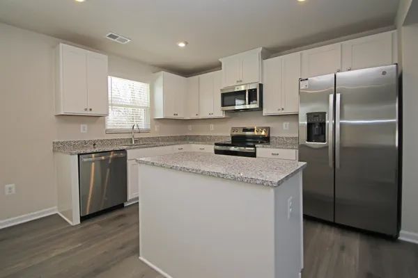 a kitchen with stainless steel appliances granite countertop a refrigerator a sink dishwasher a stove and white cabinets with wooden floor