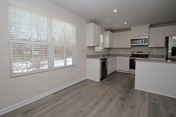 a kitchen with stainless steel appliances granite countertop a stove a sink a refrigerator white cabinets and wooden floor