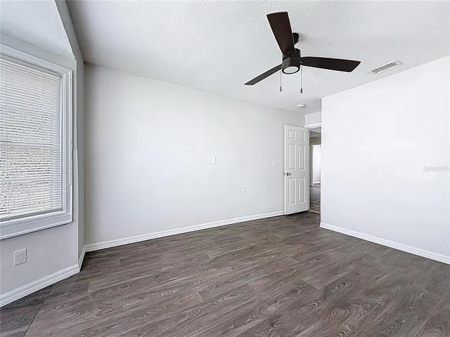 an empty room with wooden floor ceiling fan and windows