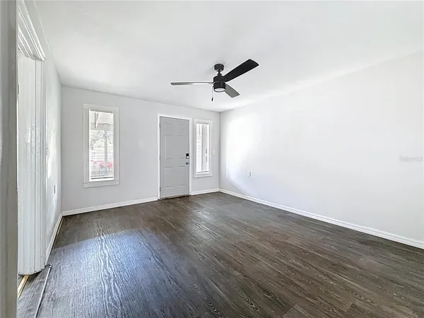 an empty room with wooden floor ceiling fan and windows