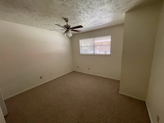 an empty room with a ceiling fan and carpet