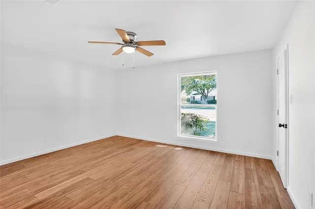 an empty room with wooden floor window and ceiling fan