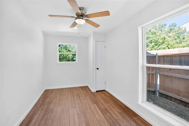 an empty room with wooden floor fan and windows