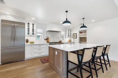 a kitchen that has a kitchen island a stove a table and chairs in it