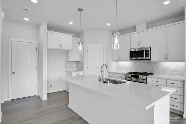 a kitchen with stainless steel appliances a stove a sink a microwave a refrigerator and white cabinets with wooden floors