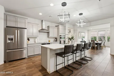 a kitchen with stainless steel appliances kitchen island granite countertop a refrigerator a stove a dining table and chairs with wooden floor