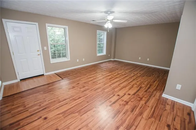 an empty room with wooden floor chandelier fan and windows