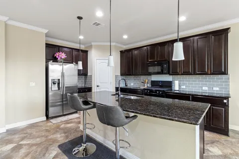 a kitchen with stainless steel appliances granite countertop a stove top oven a refrigerator a sink and chairs
