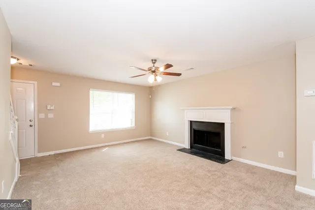 a view of an empty room with chandelier fan and fire place
