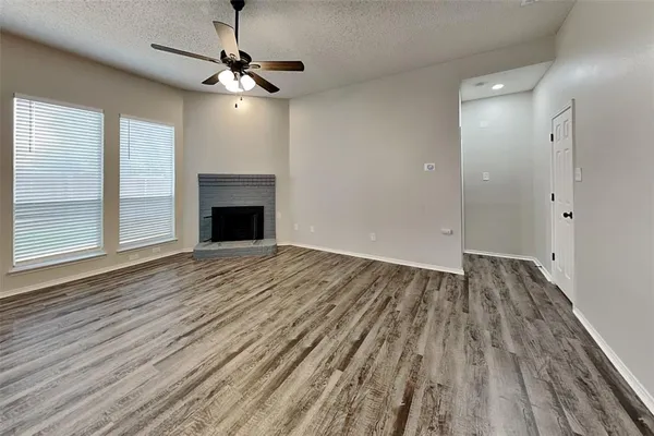 a view of an empty room with wooden floor fireplace and a window