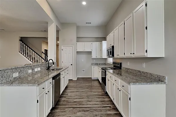 a kitchen with granite countertop a sink and dishwasher a stove top oven with wooden floor