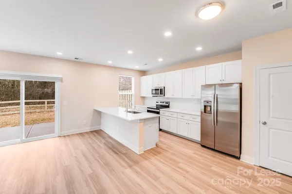 a kitchen with stainless steel appliances a stove a sink a refrigerator white cabinets and wooden floor