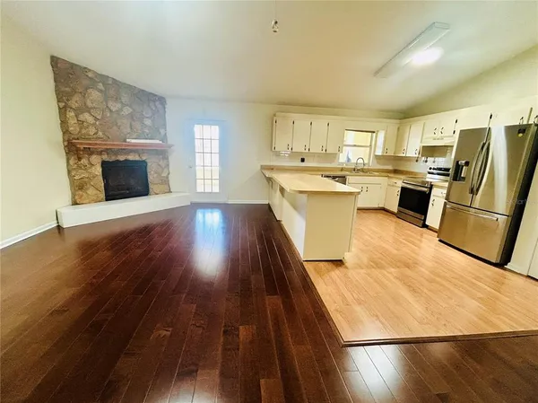 a living room with stainless steel appliances furniture a fireplace and a kitchen view