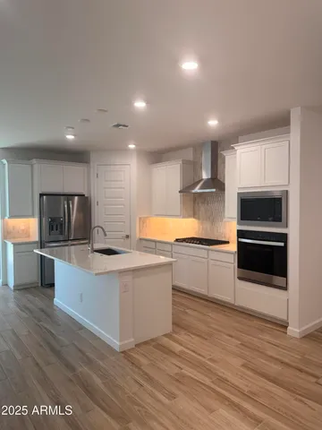a large white kitchen with stainless steel appliances kitchen island a large counter top and a stove top oven