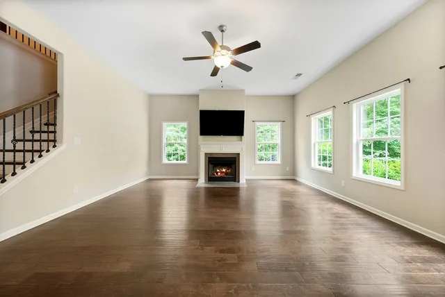 an empty room with windows a fireplace a ceiling fan and wooden floor