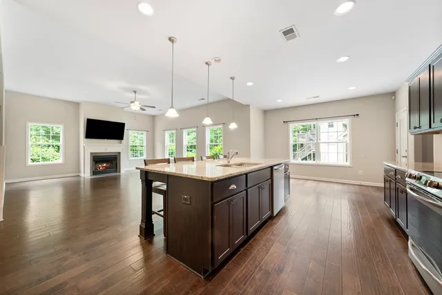 a kitchen with stainless steel appliances granite countertop wooden floors and view of living room