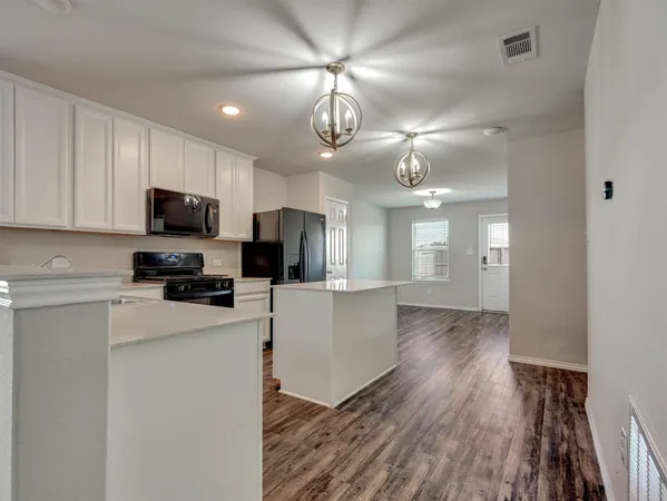 a kitchen with granite countertop a refrigerator a stove a microwave oven a sink dishwasher and white cabinets with wooden floor