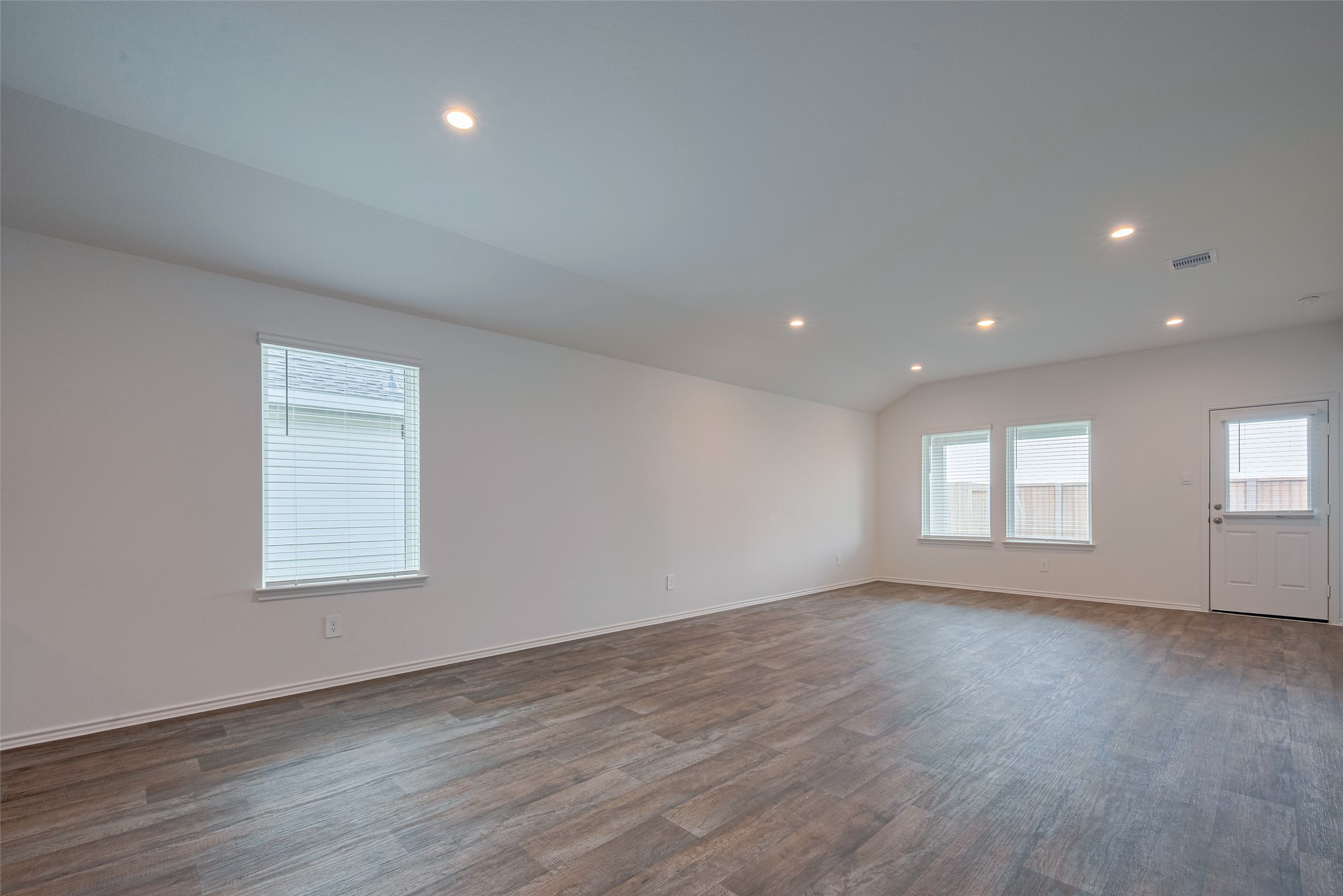30910 Rockstock Road Fulshear, TX 77441 - Photo 6 of 33 Bathed in natural light from large windows and a glass-paneled door to the backyard, the living room is bright and airy. Recessed lighting and warm-toned flooring add a cozy, modern finish.