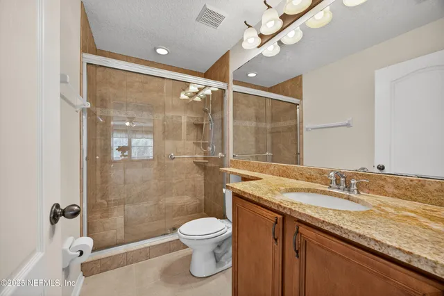 a bathroom with a granite countertop sink a toilet a mirror and shower
