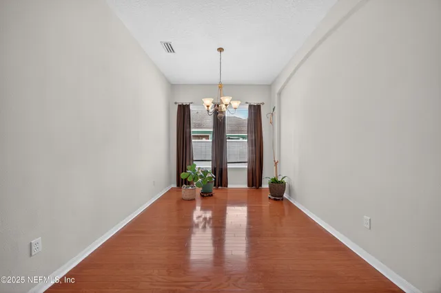 a view of an empty room with chandelier and wooden floor