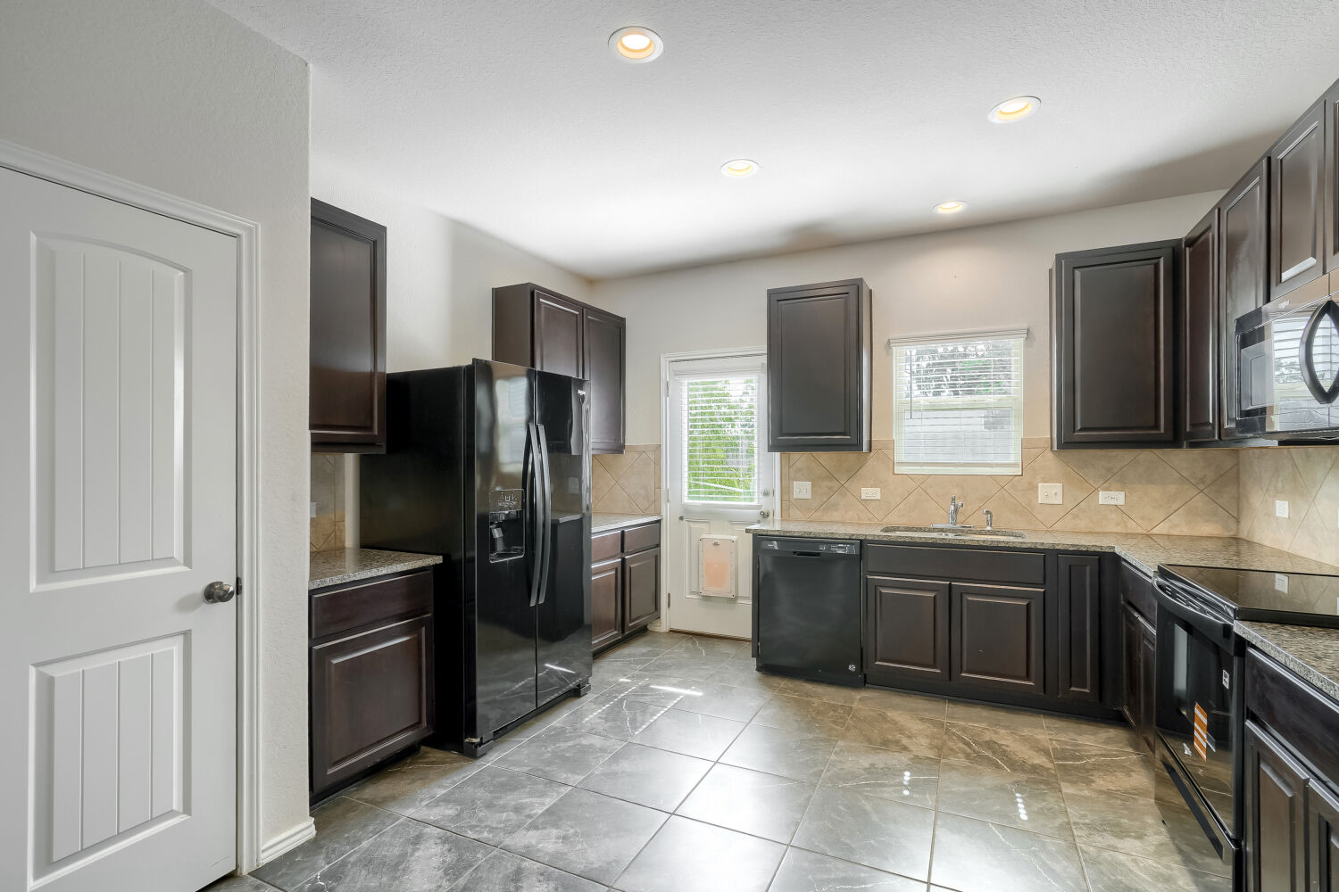 2420 Ranger Pass Seguin, TX 78155 - Photo 9 of 28 Kitchen featuring dark wood-finish cabinetry, granite-style countertops, tile backsplash, and dark tile flooring