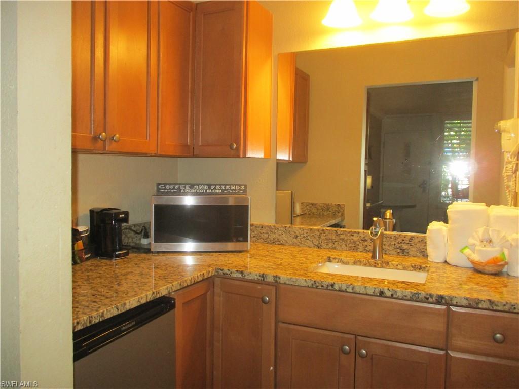 2555 9th Street North, Unit 131 Naples, FL 34103 - Photo 3 of 17 a kitchen with kitchen island granite countertop a sink stainless steel appliances wooden floor and counter space