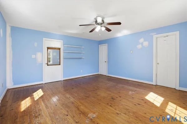 a view of an empty room with wooden floor and a ceiling fan