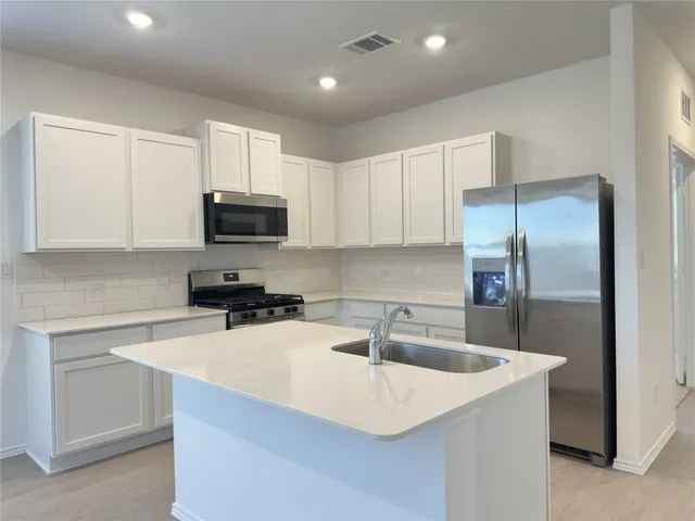 a kitchen with stainless steel appliances a sink a microwave a refrigerator and cabinets