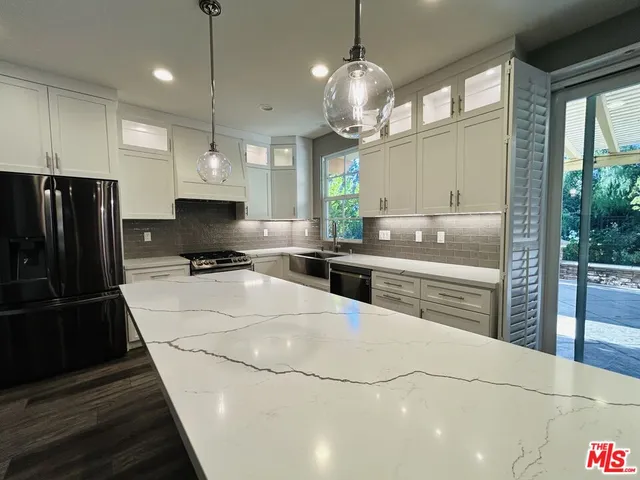 a kitchen with stainless steel appliances kitchen island granite countertop a refrigerator a sink dishwasher a stove and white cabinets with wooden floor