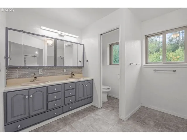 a spacious bathroom with a double vanity sink a mirror and a toilet