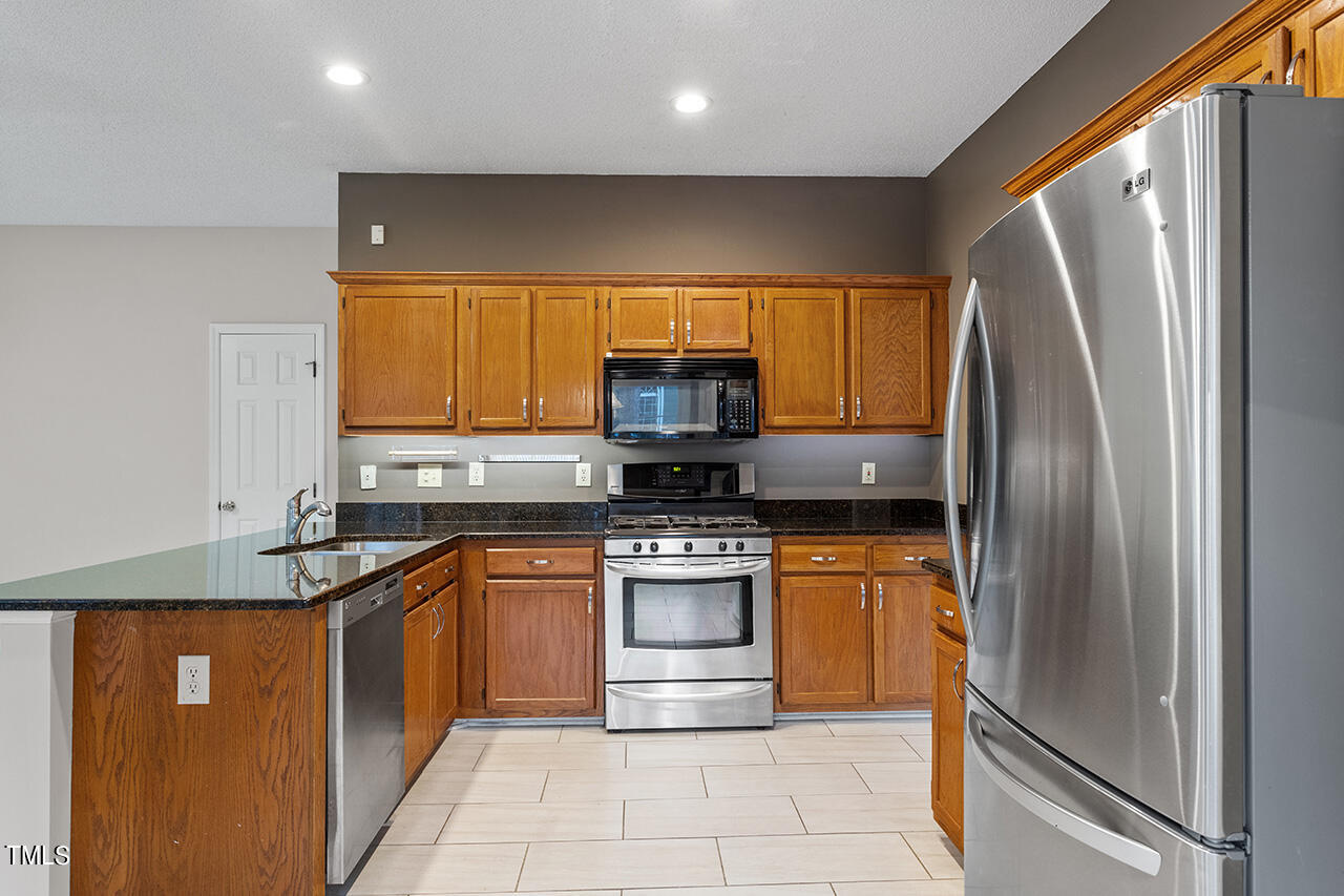 11932 North Exeter Way Raleigh, NC 27613 - Photo 17 of 35 a kitchen with stainless steel appliances granite countertop a refrigerator a stove and a sink with wooden floor
