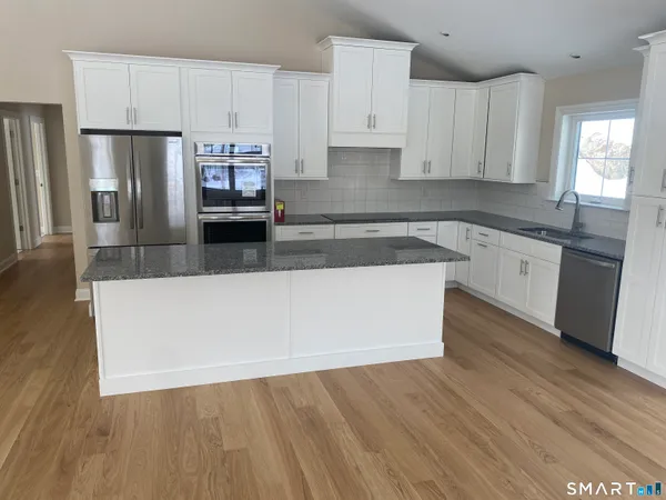 a kitchen with stainless steel appliances granite countertop a refrigerator a sink a stove and white cabinets with wooden floor