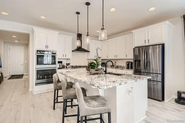 a kitchen with stainless steel appliances kitchen island granite countertop a refrigerator a stove a sink a dining table and chairs with wooden floor
