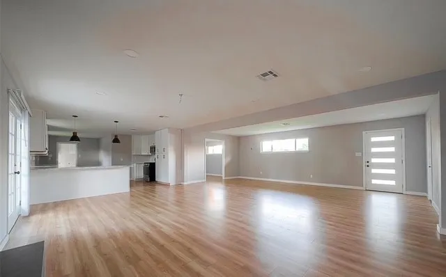 a view of an empty room and a kitchen with wooden floor