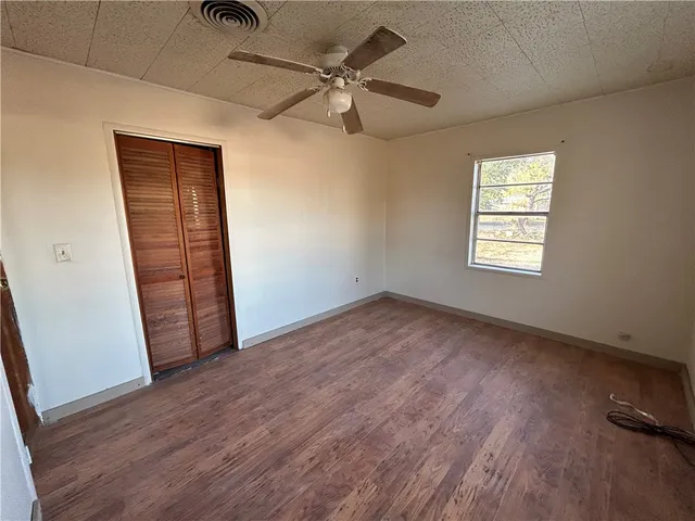 an empty room with wooden floor fan and windows