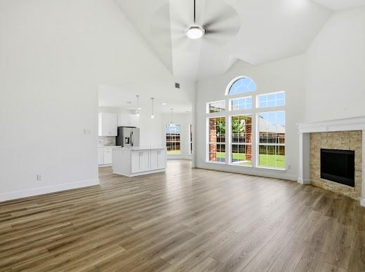 5034 West Fall Drive Midlothian, TX 76065 - Photo 12 of 40 Spacious living area featuring wood-finish flooring, a vaulted ceiling with a modern ceiling fan, and a stone-surround fireplace with a classic mantel