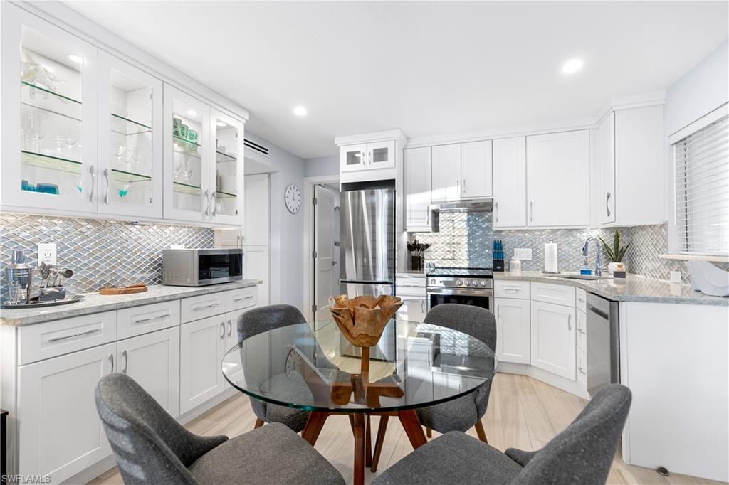 175 5th Avenue South, Unit 3 Naples, FL 34102 - Photo 13 of 31 a kitchen with stainless steel appliances granite countertop a stove a sink dishwasher a dining table and chairs with wooden floor