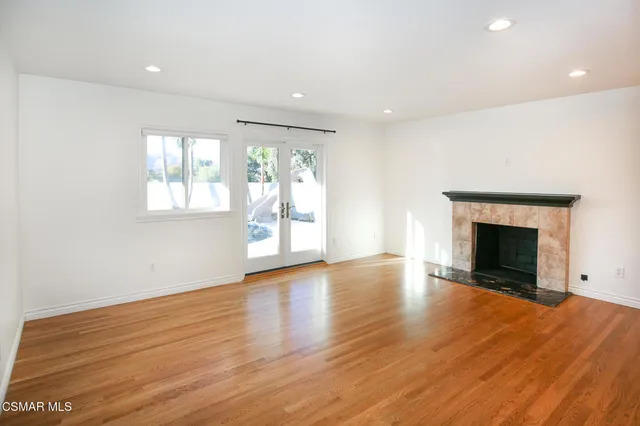 an empty room with wooden floor fireplace and windows