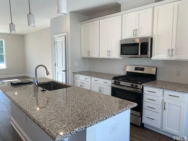 a kitchen with granite countertop a sink stove and white cabinets