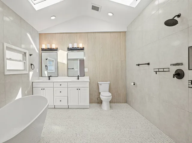 a spacious bathroom with a double vanity sink a mirror a toilet and a bathtub