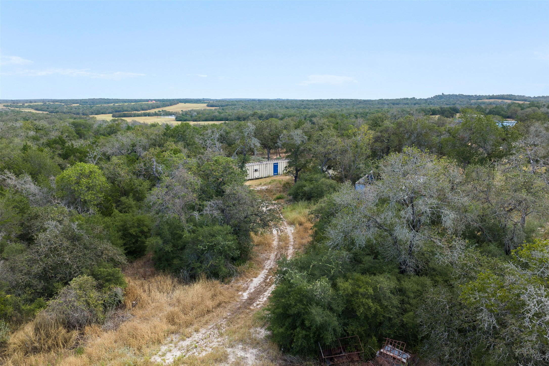 3301 Chuckwagon Road Harwood, TX 78632 - Photo 1 of 36 A winding dirt road cuts through dense woods under a wide open sky.