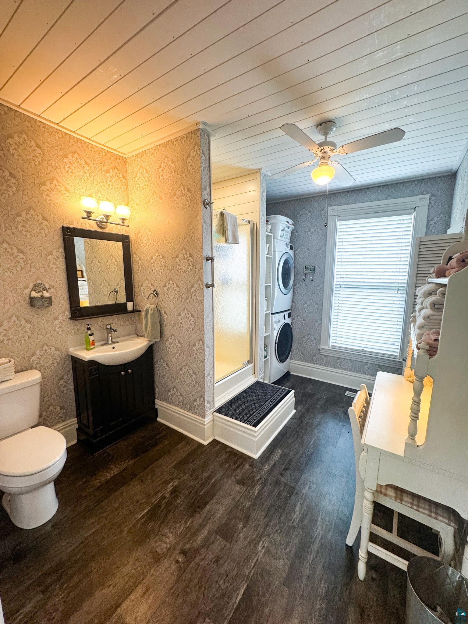 303 East 5th Street Washburn, WI 54891 - Photo 24 of 34 Bathroom featuring wood-finish flooring, a wall-mounted vanity with a black cabinet, a glass shower enclosure, a stacked washer and dryer, and a ceiling fan