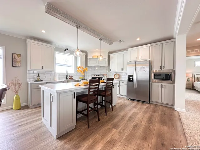 a kitchen with stainless steel appliances a refrigerator a stove a sink dishwasher and a dining table with wooden floor