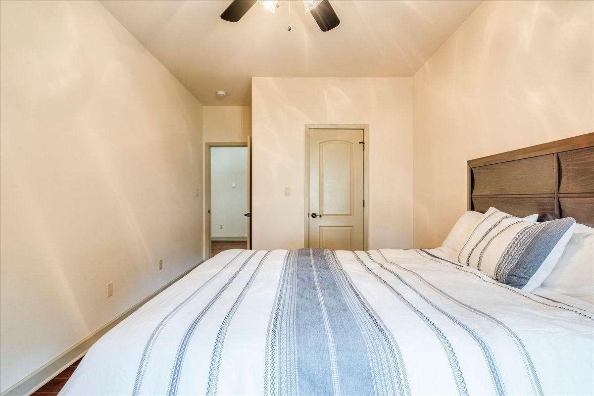 3012 South 4th Street, Unit B Austin, TX 78704 - Photo 20 of 40 Bedroom featuring a wood-finish headboard, neutral wall paint, wood-finish flooring, a ceiling fan, and a paneled door with a black knob
