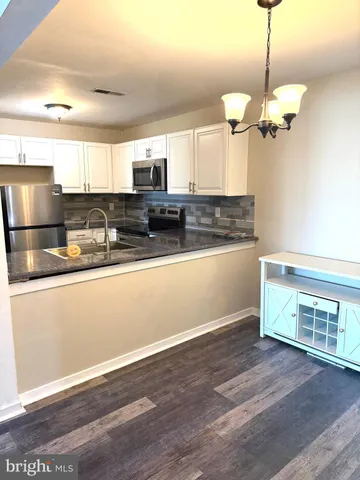 a kitchen with stainless steel appliances granite countertop a refrigerator a sink dishwasher a stove and white cabinets with wooden floor