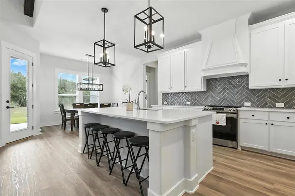 a kitchen with stainless steel appliances granite countertop a sink a stove a dining table and chairs with wooden floor