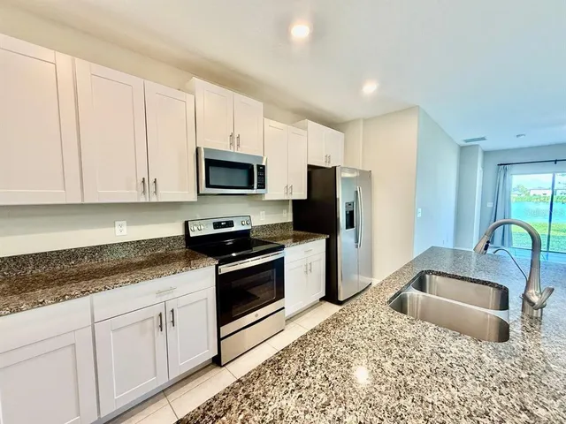 a kitchen with granite countertop a sink a stove a microwave a refrigerator and white cabinets