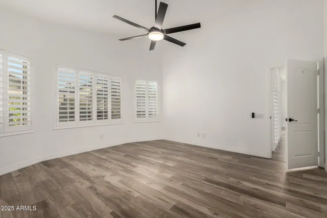 an empty room with wooden floor fan and windows