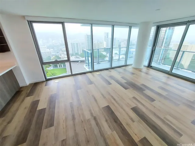 a view of an empty room with wooden floor and a hallway